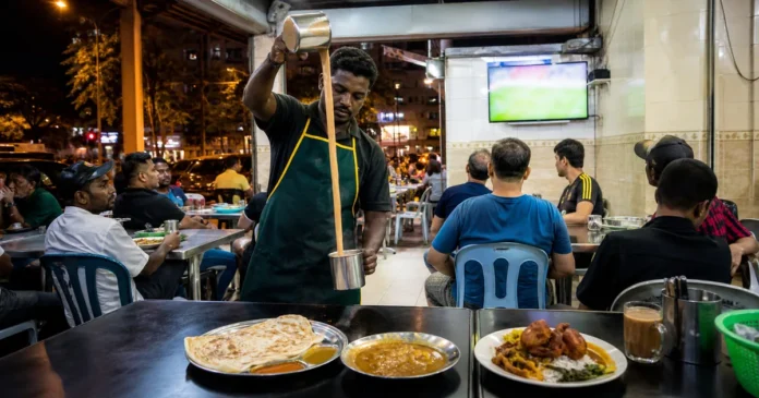 Server pulling teh tarik beside roti canai and nasi kandar in a busy Kuala Lumpur mamak after midnight
